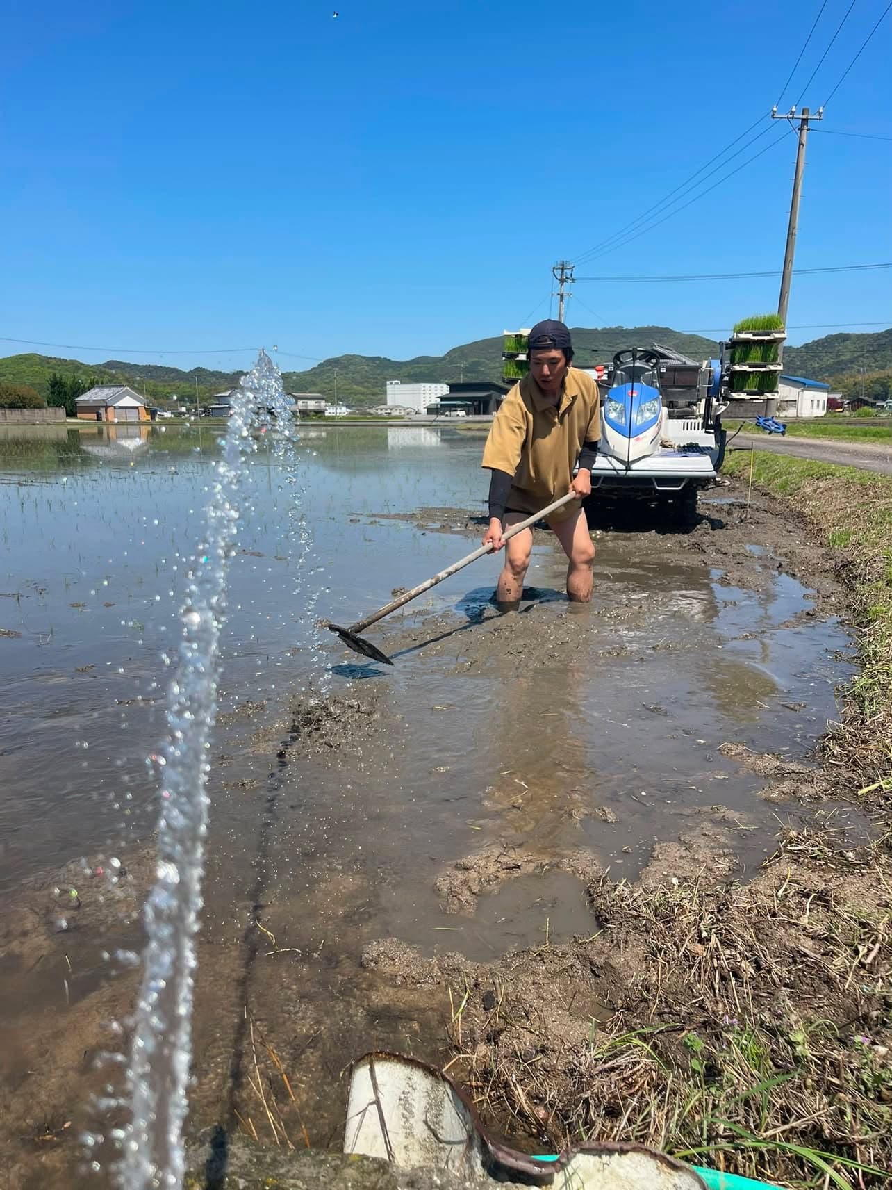 田植えの日、水を張った田んぼで代かきの仕上げをする坂下頌平